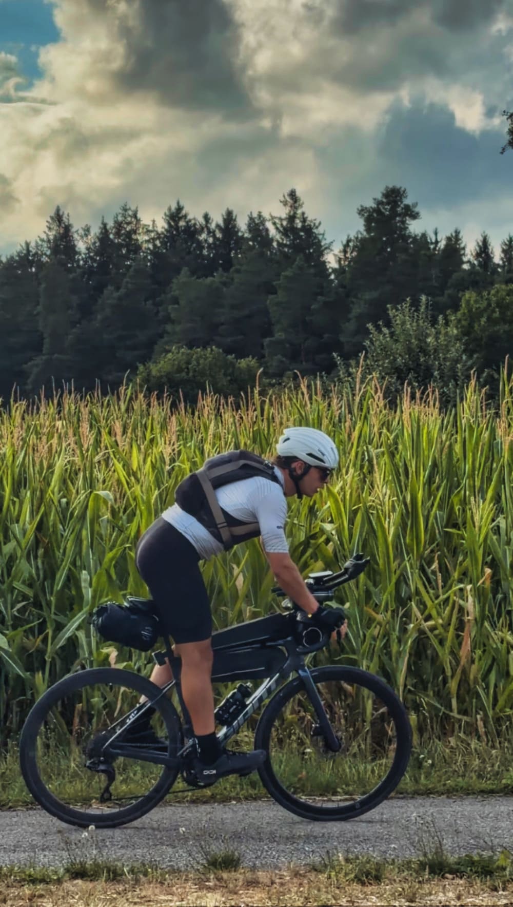 Cycliste en tenue Ozio roulant devant un champ de maïs lors de la Nomadian 2026